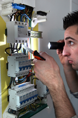 Electrician examining a fusebox with a torch